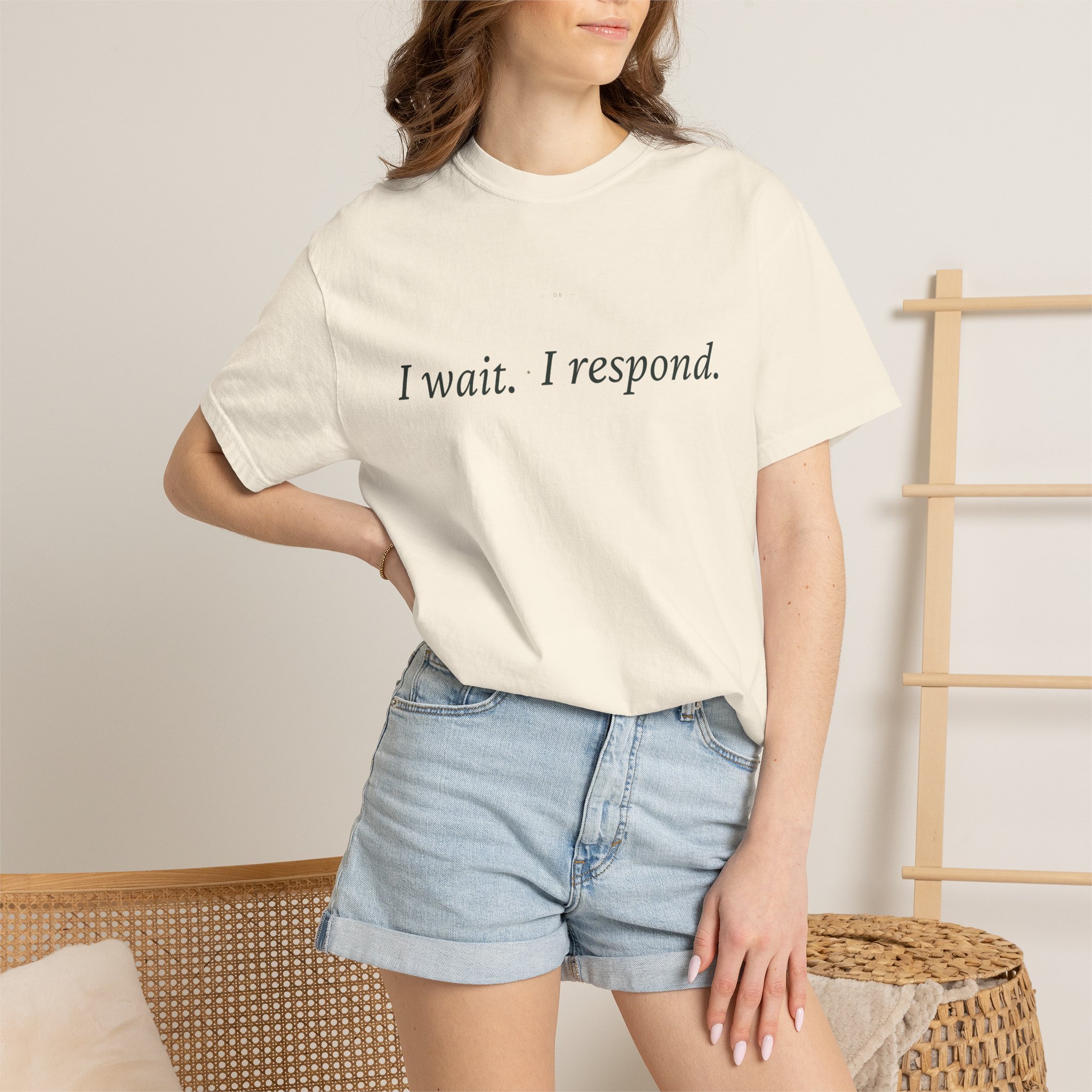 Partial view of a person wearing a white T-shirt with the text 'I wait. I respond.', paired with light denim shorts, seated beside a woven basket.