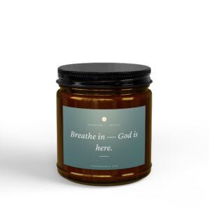 Close-up of a dark amber glass bottle with a black screw cap; label reads 'Breathe in — God is here' on a blue gradient background.