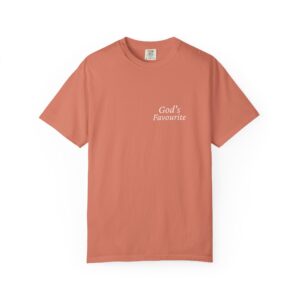 Peach-colored T-shirt laid flat with a visible clothing tag at the neckline and white text on the chest reading "God's Favourite" (partially obscured).