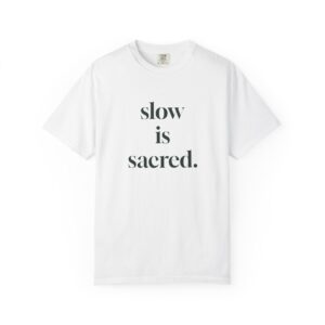 White crew-neck T-shirt with bold black text: “slow is sacred.”