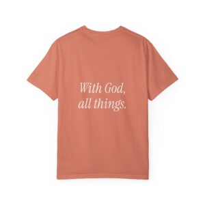 Back view of a coral-colored t-shirt showing white cursive text: 'With God, all things' (partial view).