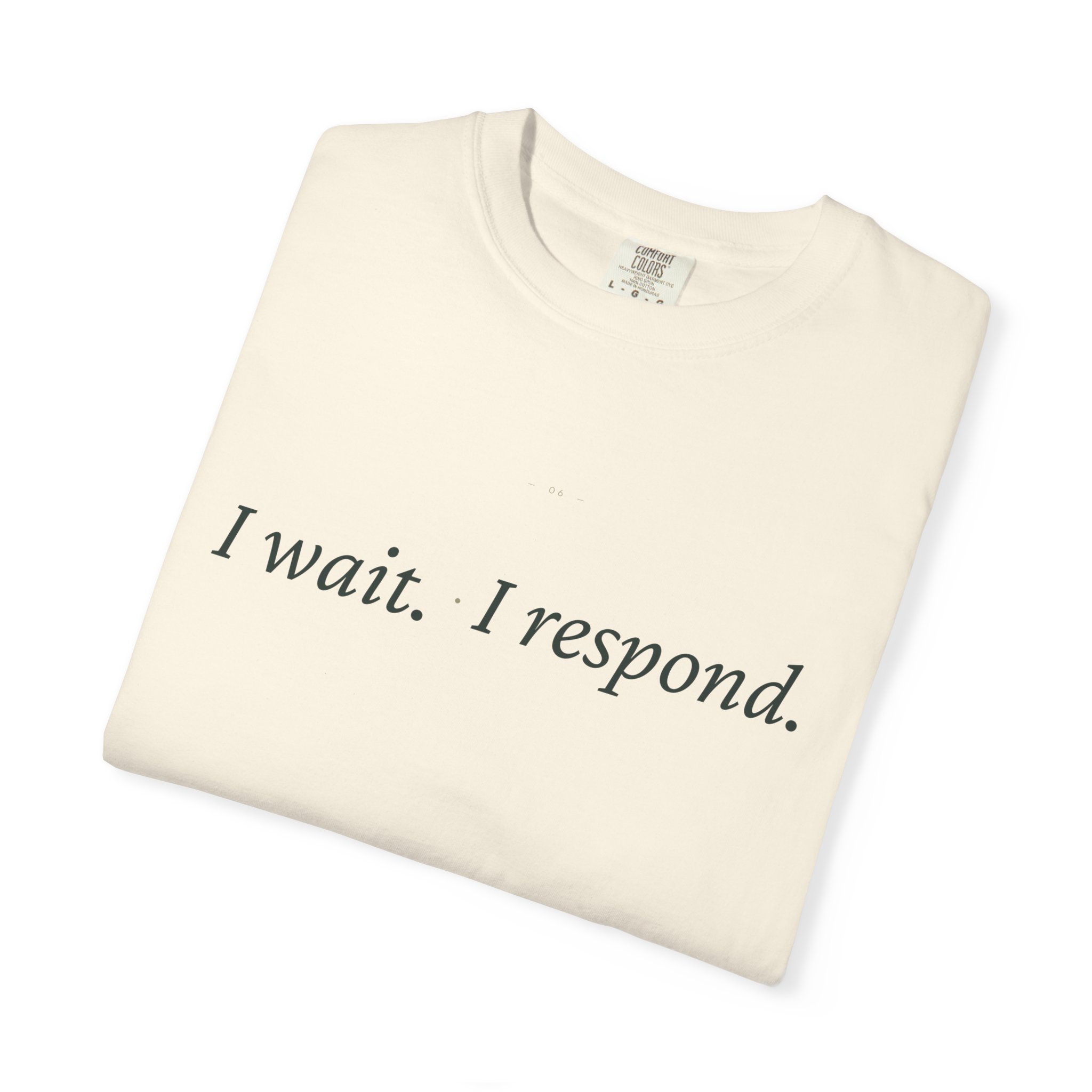 Cream-colored T-shirt folded at an angle, with a visible collar tag and partial front print reading 'I wait...'.